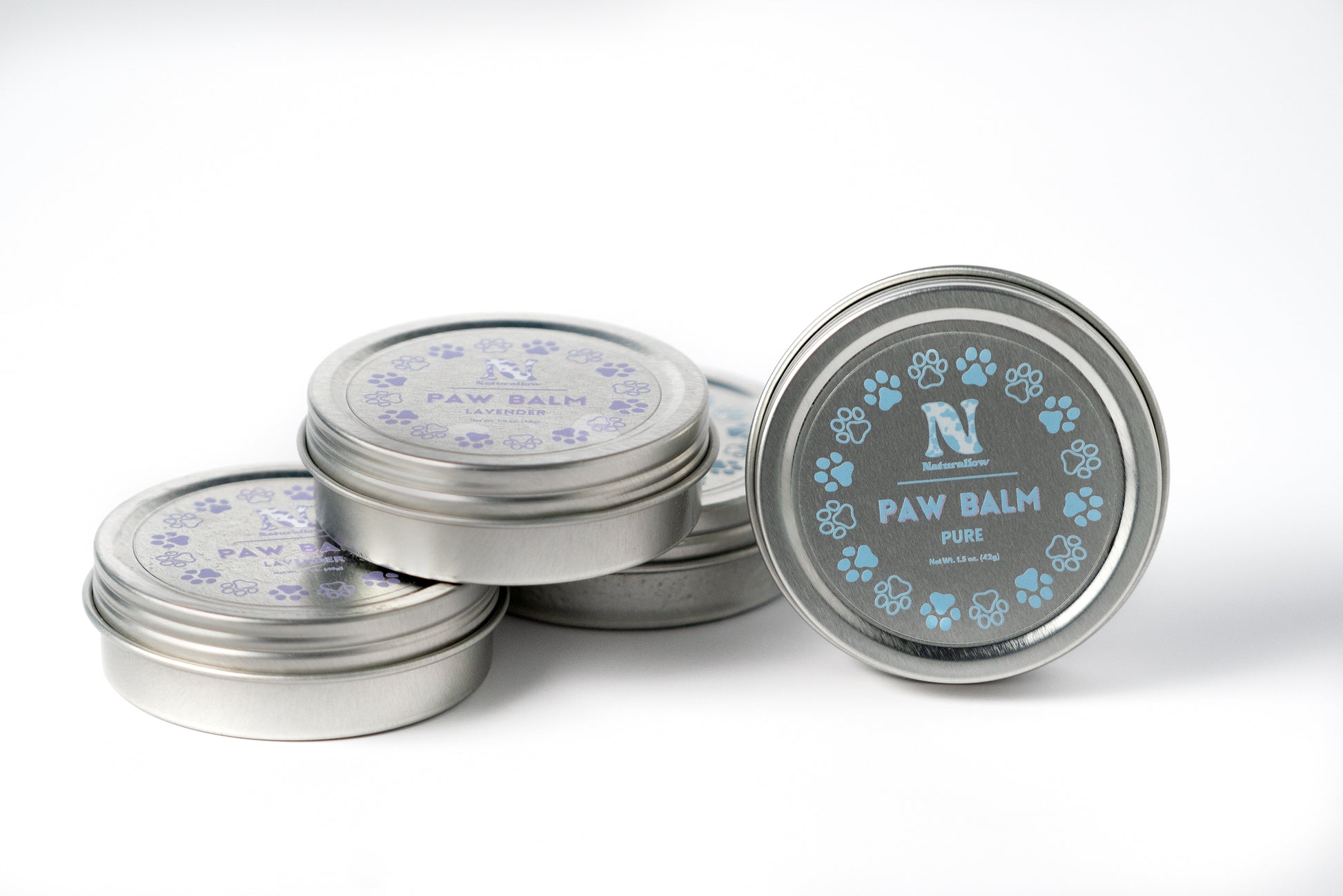 A photo of a stack of small, circular tins with a tin standing on its own to the right that has light blue paw print illustrations. Its label reads "Naturallow Paw Balm Pure. Net Weight 1.5 oz (42g)"